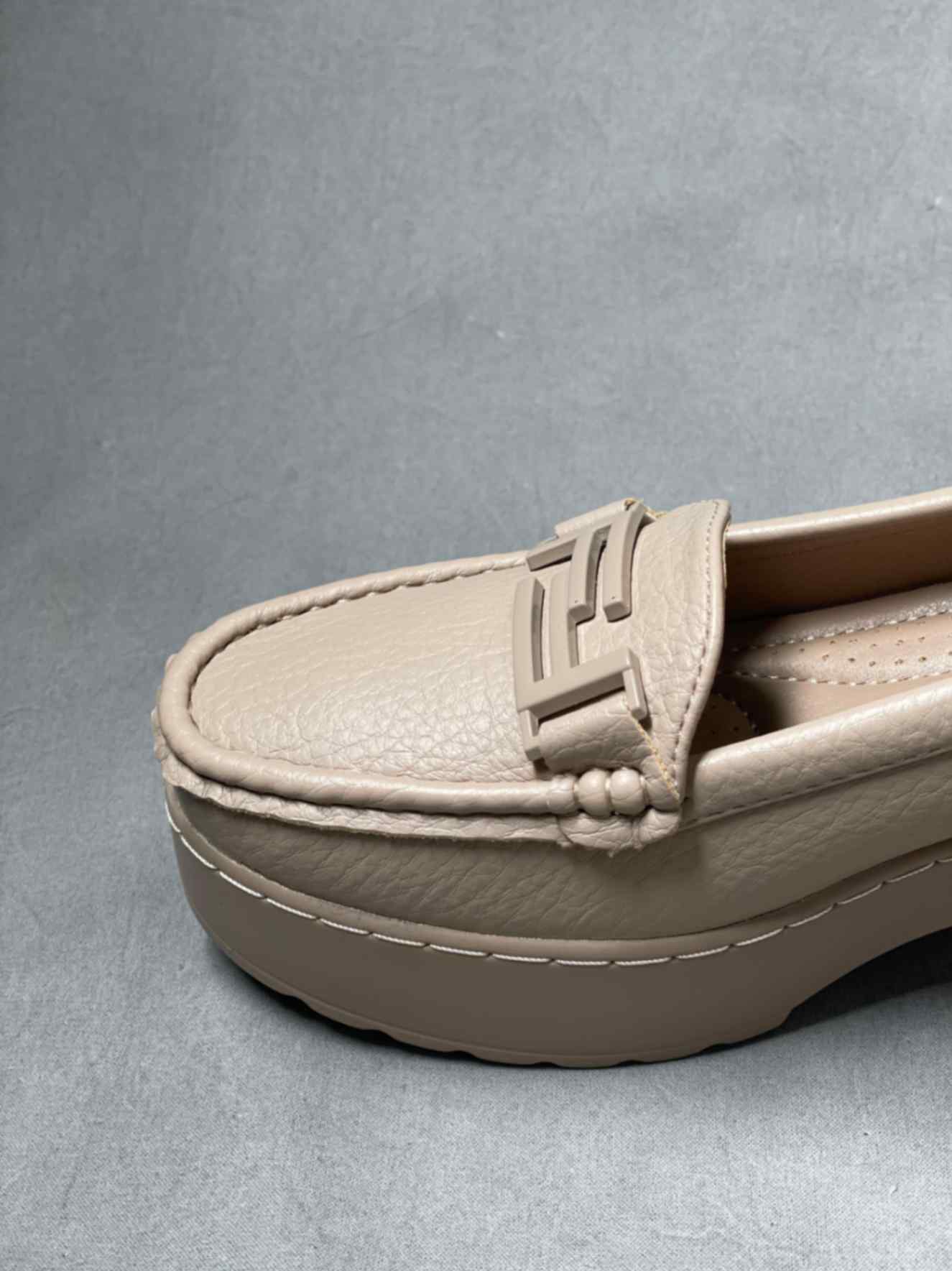 Close-up of beige heeled loafers with buckle, emphasizing the textured material and elegant buckle detail on the upper.