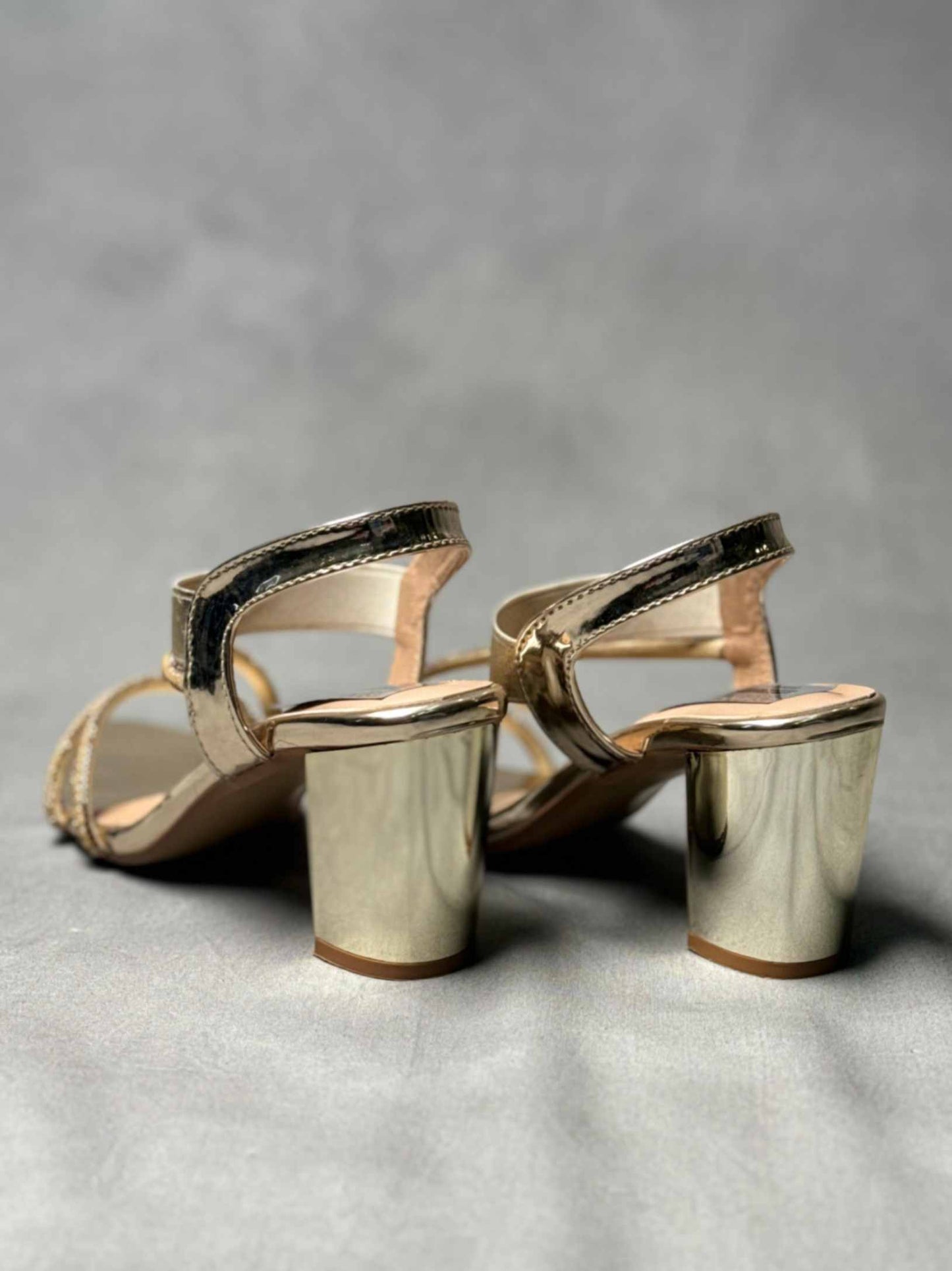 Back view of golden block heels featuring a metallic finish and secure ankle straps, designed for comfort and style.