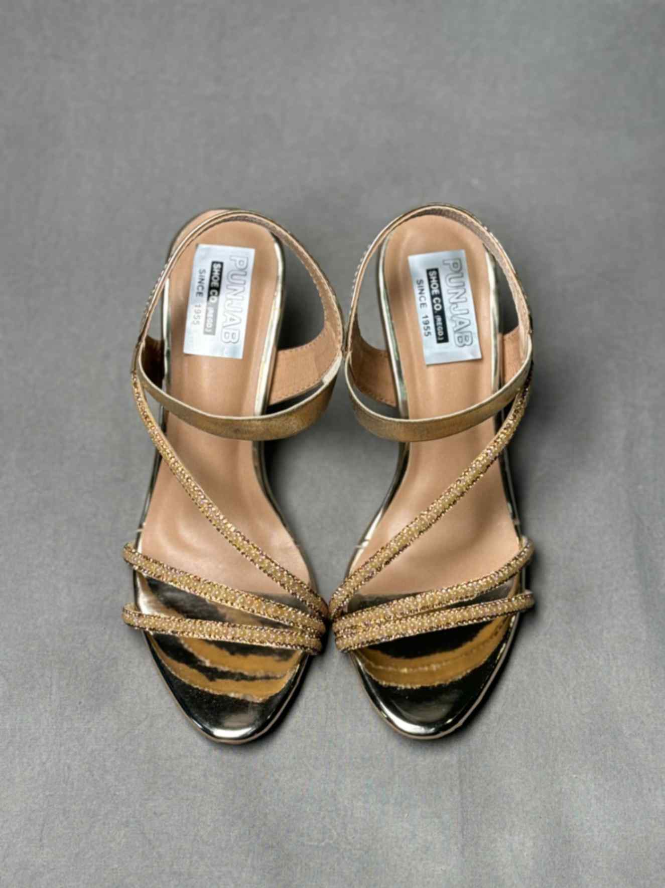 Pair of golden heels with adjustable ankle straps, glittery detailing, and a pointed toe, ideal for women’s evening attire.